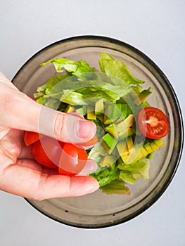 Close up of female chef hand putting Feta cheese cubes on greek vegan tomato salad with olives and lettuce leaves. The concept of