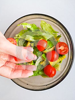 Close up of female chef hand putting Feta cheese cubes on greek vegan tomato salad with olives and lettuce leaves. The concept of