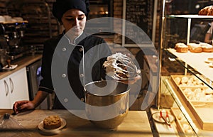 Close-up of a female chef holding an egg whisk with whipped cream. Metal bowls with sweet delicious cream in the