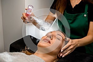 close-up of female client and beautician gently moisturizes her face with steam from portable humidifier