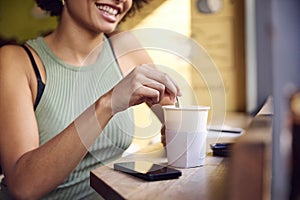 Close Up Of Female Customer In Window Of Cafe Stirring Hot Drink In Takeaway Cup With Wooden Stirrer