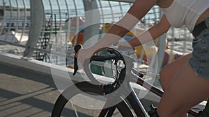 Close up of female cyclist hands on handlebar of road bike. Woman is riding bicycle along beach boardwalk in sunlight. Girl rides