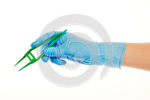 Close up of female doctor's hand in blue sterilized surgical glove with green plastic forceps against white