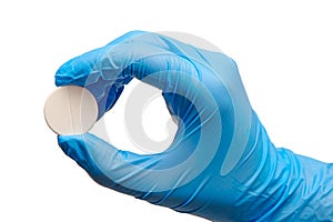 Close up of female doctor's hand in blue sterilized surgical glove holding big round white tablet