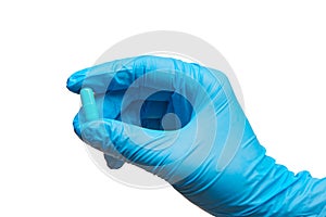 Close up of female doctor's hand in blue sterilized surgical glove holding blue capsule