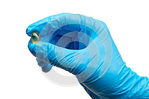 Close up of female doctor's hand in blue sterilized surgical glove holding yellow tablet