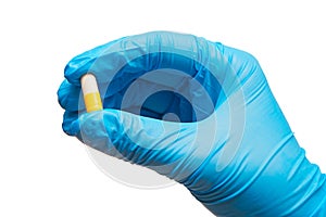 Close up of female doctor's hand in blue sterilized surgical glove holding yellow and white capsule