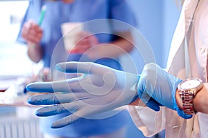 Close up of female doctor's hands putting on blue sterilized surgical gloves in the medical clinic.