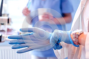 Close up of female doctor's hands putting on blue sterilized surgical gloves in the medical clinic.