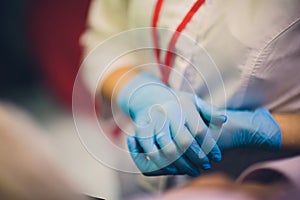 Close up of female doctor`s hands putting on blue sterilized surgical gloves in the office.