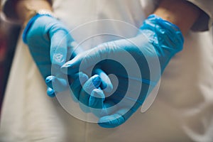 Close up of female doctor`s hands putting on blue sterilized surgical gloves in the office.