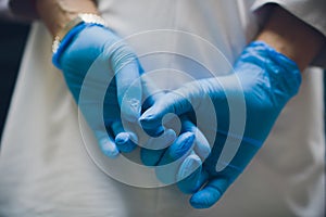 Close up of female doctor`s hands putting on blue sterilized surgical gloves in the office.