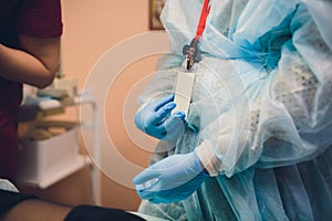 Close up of female doctor`s hands putting on blue sterilized surgical gloves in the office.