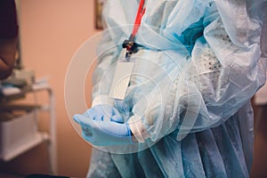 Close up of female doctor`s hands putting on blue sterilized surgical gloves in the office.