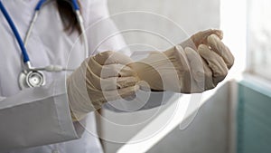 Close up of female doctor`s hands putting on sterilized surgical gloves in the office.