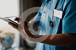 Close-up of female doctor in scrubs with digital tablet, typing and completing checklist