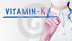 Close up female doctor writing word VITAMIN K with marker. Medical concept