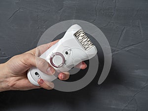 Close-up of a female electric epilator in a female hand on a gray textured background