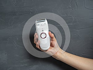 Close-up of a female electric epilator in a female hand on a gray textured background
