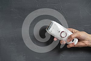 Close-up of a female electric epilator in a female hand on a gray textured background. Copy space