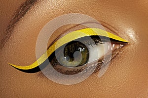 Close-up Female Eye with bright yellow Eyeliner Makeup. Neon Disco make-up with black liner. Summer beauty style