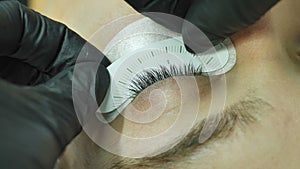 Close-up female eye with substrate on the eyelid of a beauty salon master applies a stencil measuring the size of