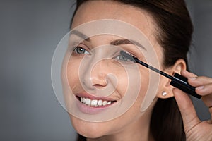 Close up female face holding tube applying black mascara