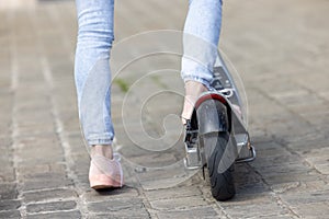 Close-up of female feet of a girl wearing pink sneakers and a jeans on an electric scooter on the background of the city