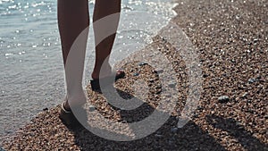 Close-up of female feet shod in flip flops shoes walking on sea beach