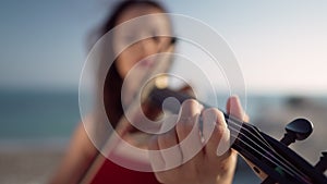 Close-up female finger on violin violin fretboard with blurred Caucasian musician playing with bow at background