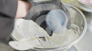 Close-up of female hand adding food dye to confectionery topping in metal bowl. Unrecognizable Caucasian young baker