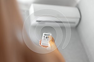 Close-up of female hand adjusting air conditioner with remote control.