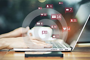 Close up of female hand with coffee cup using laptop at desktop with social media icons on blurry outdoor background.