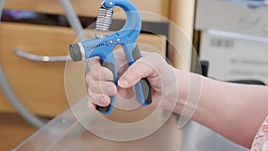 close-up female hand compresses spring expander, disabled elderly woman 75s after stroke trains muscles of hand, motor skills