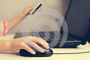 Close up of female hand on computer mouse and holding a credit card.