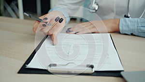 Close-up of female hand doctor writing in patient`s chart ticking symptoms in office