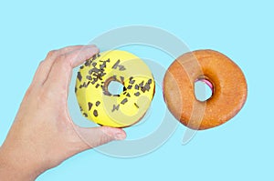 Close-up of a female hand grabs one of two donuts on a blue background. View from above.