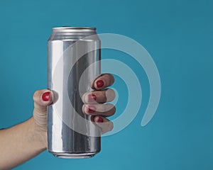 Close-up of female hand holding aluminum can of beverage, beer, soda or soft drink. On light blue background. Copy space