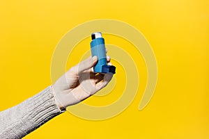 Close-up of female hand holding asthmatic inhaler on yellow background.