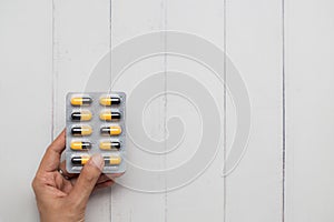 Close up of female hand holding blister pack of pills on white wooden background