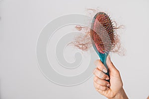 Close-up of a female hand holding a comb with a bun of hair on a white background. Hair loss and female alopecia