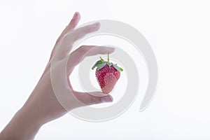 A female hand holding a fresh looking strawberry on a light background.Healthy food and lifestyle concept
