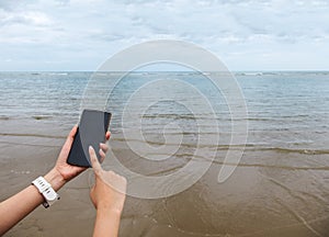 Close up of Female Hand Holding Smart Mobile Phone with Blank Screen on The Beach with Clear Sky, Beach Sand and Wave used as Temp