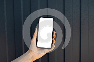 Close-up of female hand holding smartphone with blank on screen, on background of black metal facade of modern house. Mockup