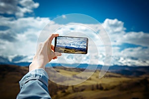 Close-up of female hand holding smartphone and taking photo or video. Woman traveler on the background of a snowy mountain range