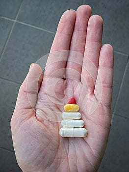 Close-up of a female hand holding a variety of colorful pills in her palm looks like a Christmas tree.