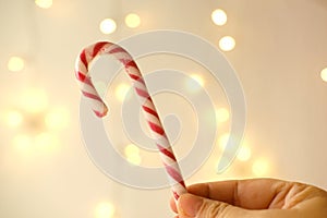 Close-up female hand holds candy cane, traditionally white with red stripes cane-shaped stick candy, Christmastide, Saint Nicholas