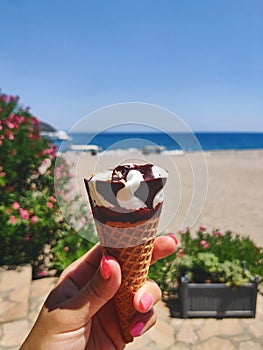 Close up. A female hand holds an ice cream cone. Against the backdrop of the beach and the Mediterranean Sea