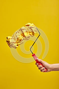 Close up of female hand holds paint roller for wall painting isolated on yellow background