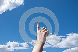 Close-up female hand with index finger up on a background of blue sky with clouds, copy space